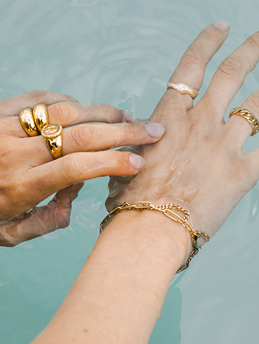 Hände im Wasser mit goldenen Ringen und Armschmuck